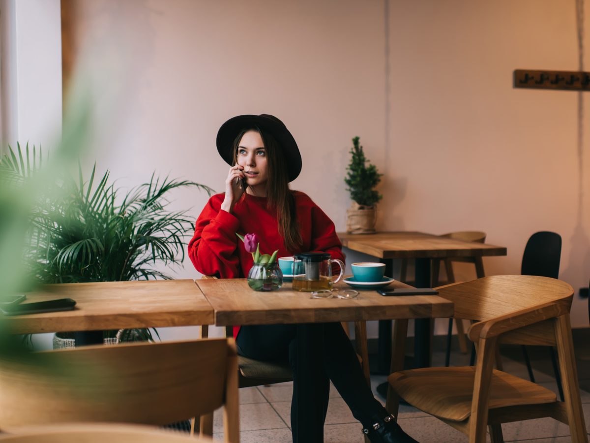 A woman on the phone at a window table, a pot of tea and a cup in front of her