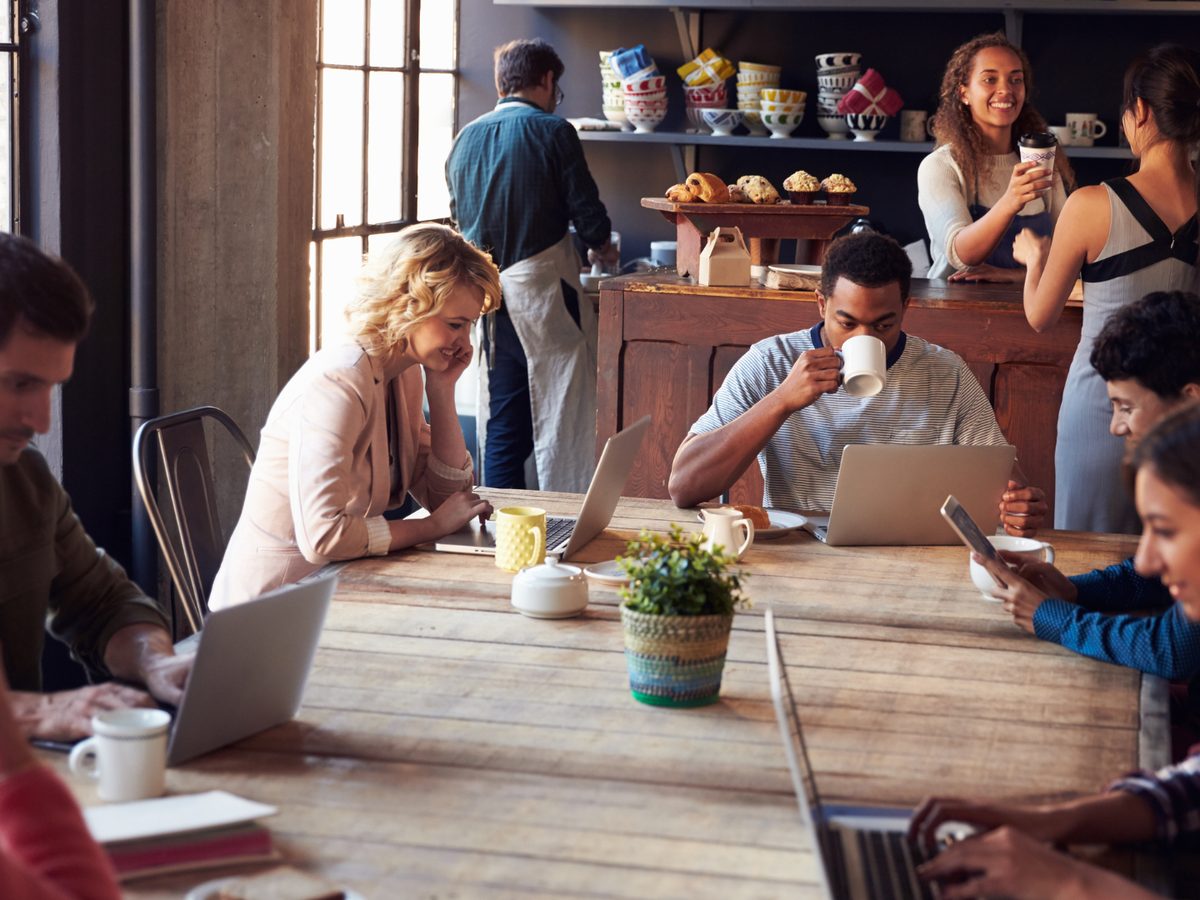 A long communal table, laptops and mugs down both sides