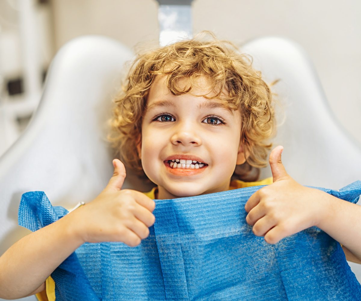 A child in the dentist's chair giving a thumbs up