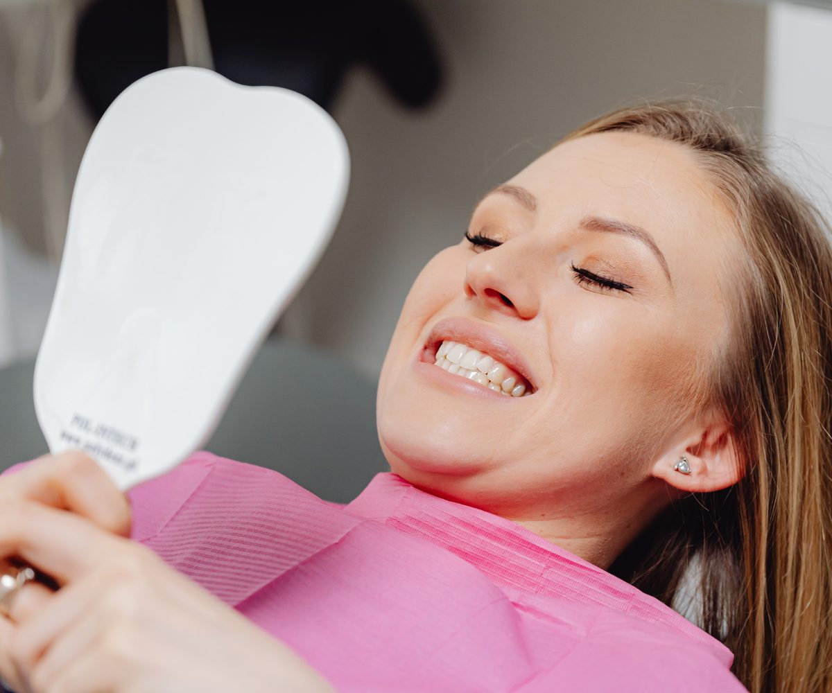 A patient in the chair looking at her teeth in a hand mirror