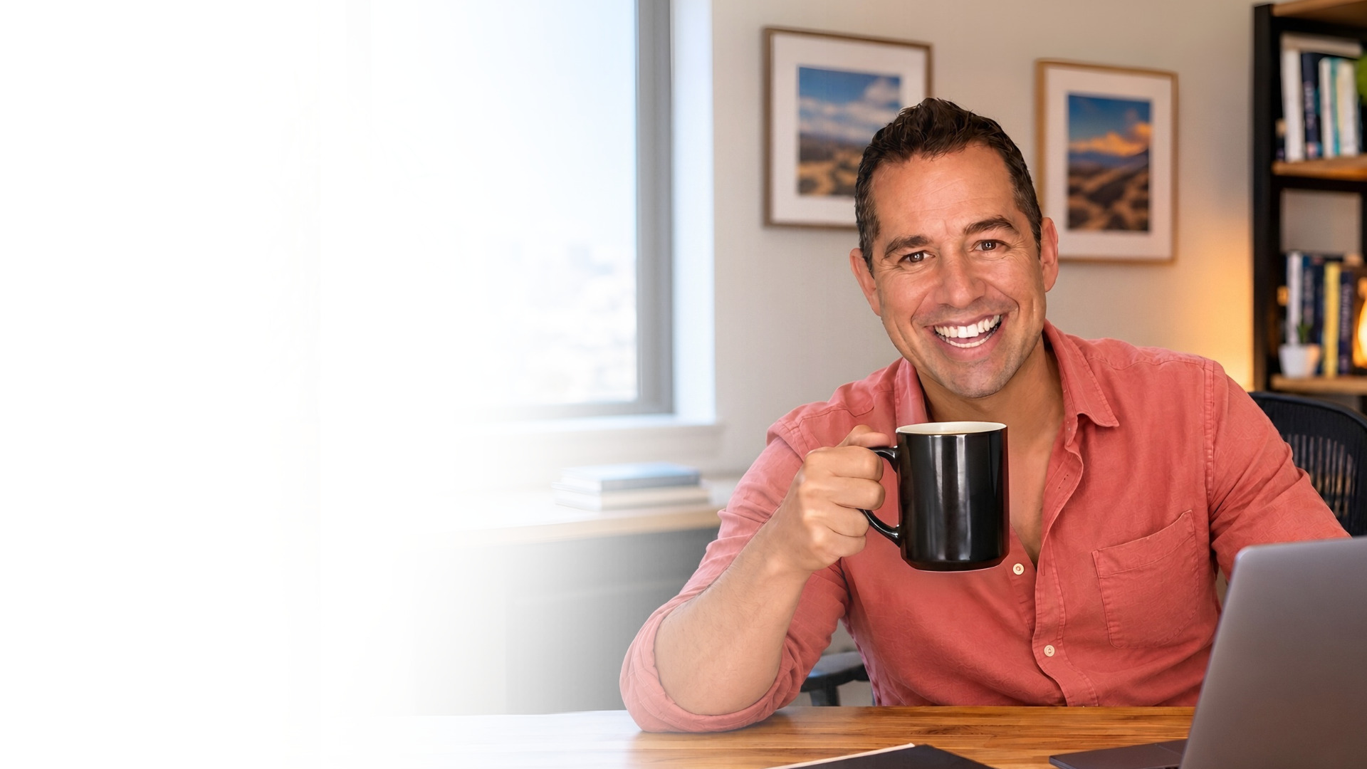 Oz Luv at his desk in a pink shirt, smiling, raising a coffee mug